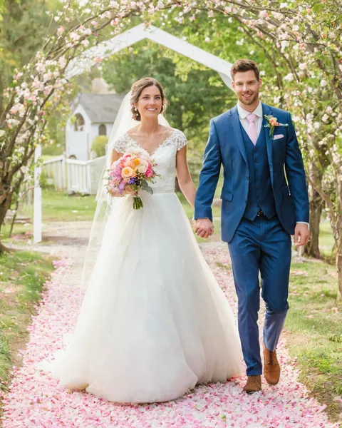 A bride and groom walking down a pink petal path under blooming trees.