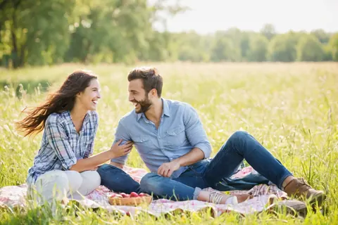 A happy couple laughing while having a picnic on a grassy field with apples.