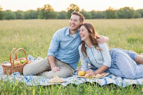 A smiling couple enjoying a picnic on a blanket in a grassy field.