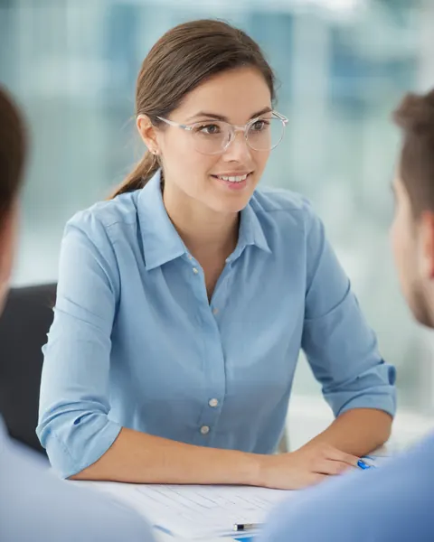 A woman wearing glasses and a blue shirt smiles during a business meeting.