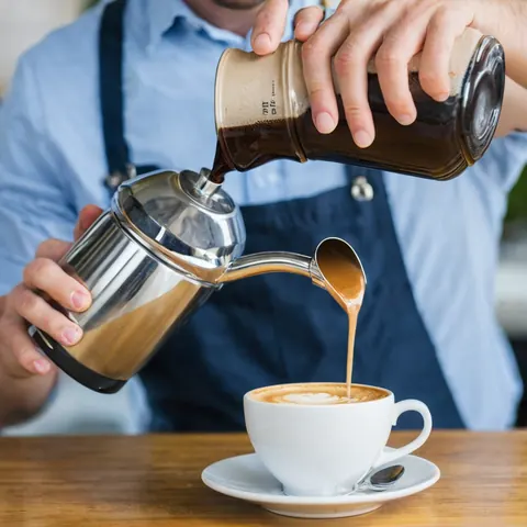 Barista pouring coffee into a cup with latte art on a wooden table