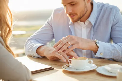 Man holding woman's hand over coffee cup at outdoor table in sunlight