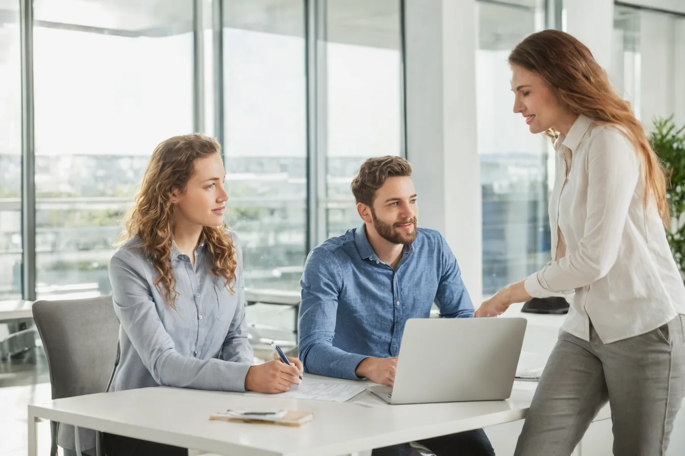 Three colleagues in a modern office collaborating around a laptop during a business meeting.