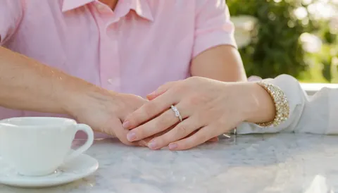 Two hands clasped together on a marble table with a coffee cup nearby.