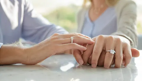 Two hands with diamond rings clasped together on a marble surface.
