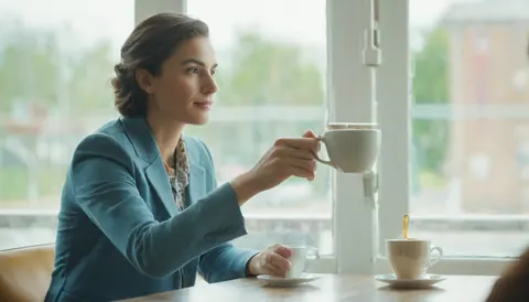 Woman in teal blazer sipping coffee by window in cafe